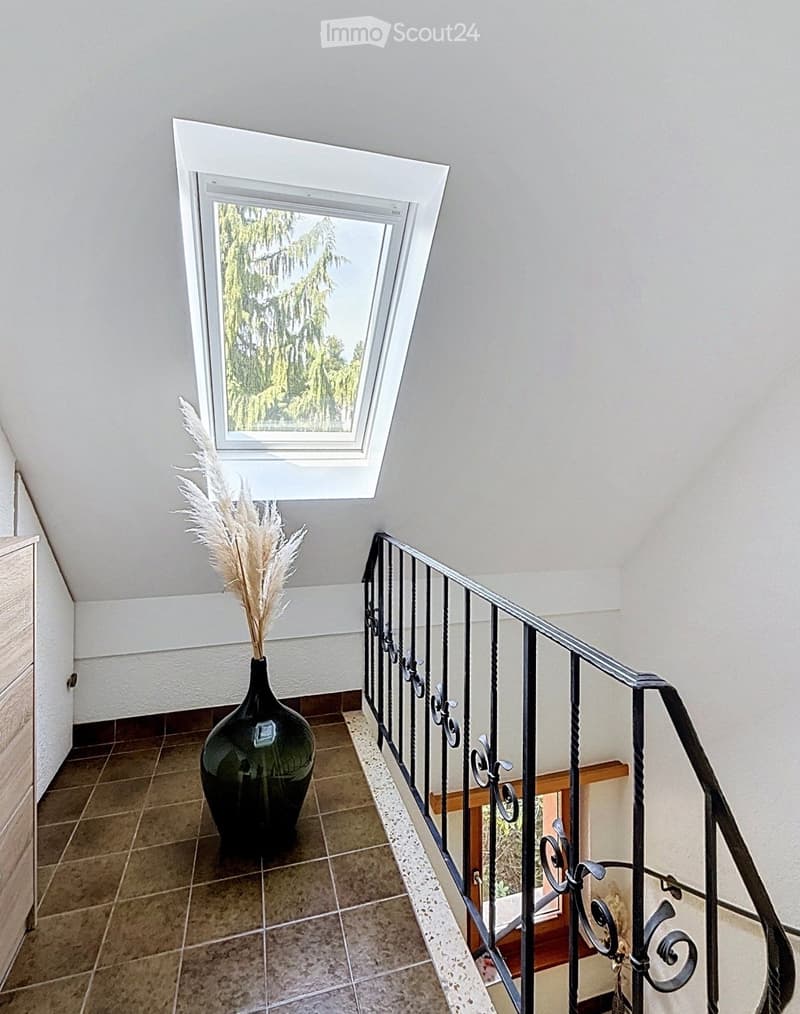 Staircase with a black wrought iron railing, a green vase with dried plants on the landing, and a skylight window above.