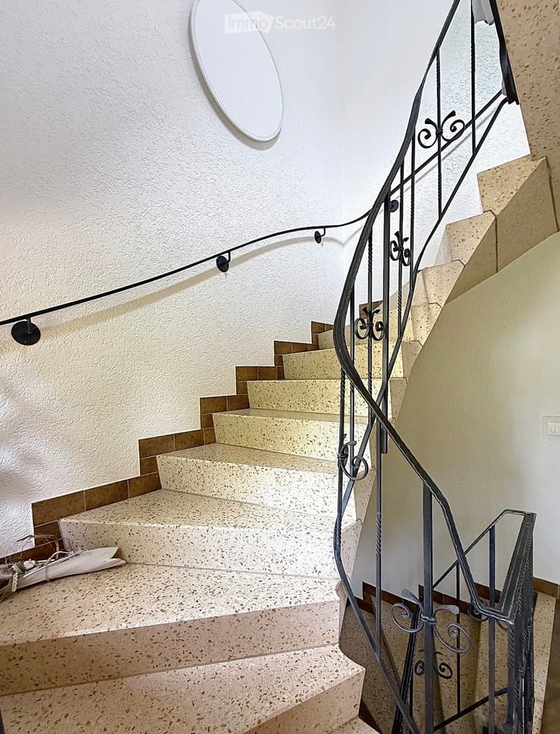 Spiral staircase with beige marble steps and a black wrought iron railing, featuring a decorative mirror on the wall above.