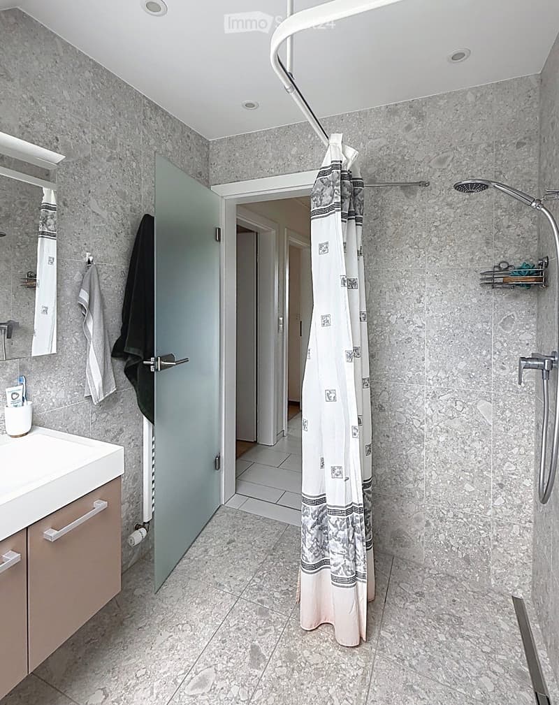 Modern bathroom with marble tiles, a white sink, a glass shower enclosure, and a patterned shower curtain.