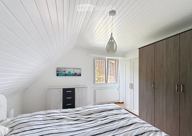 Modern bedroom with white walls, wooden floor, bed with striped bedding, large wardrobe, dresser with drawers, and a pendant light fixture.