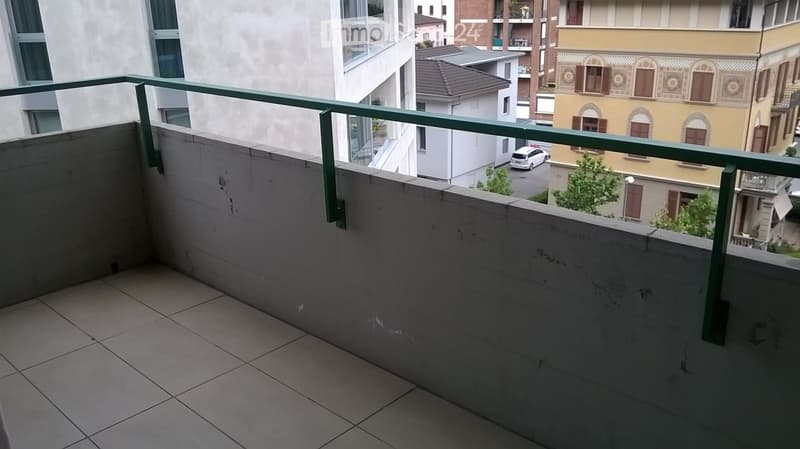 Balcony with tiled floor and green metal railing, overlooking a cityscape with buildings and parked cars.