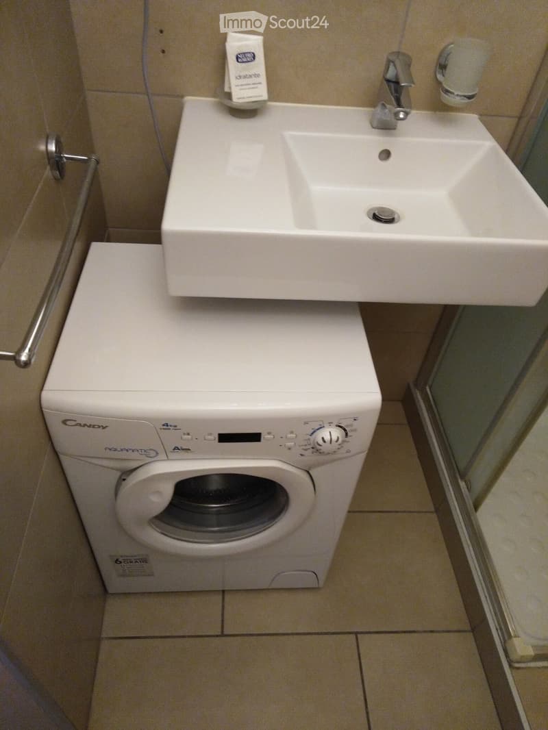 Bathroom with a white sink, faucet, and a white washing machine below it.