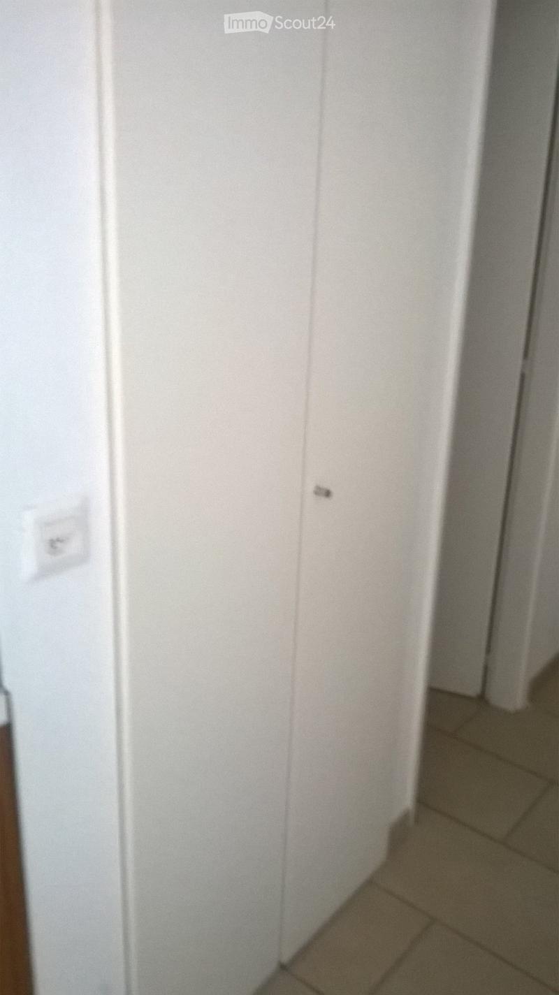A narrow, empty hallway with white walls and tiled flooring, featuring a light switch on the left wall.