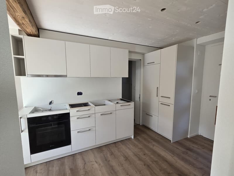Modern kitchen with white cabinets, stainless steel handles, and a built-in oven. The space features wooden flooring and an open layout with visible storage compartments.
