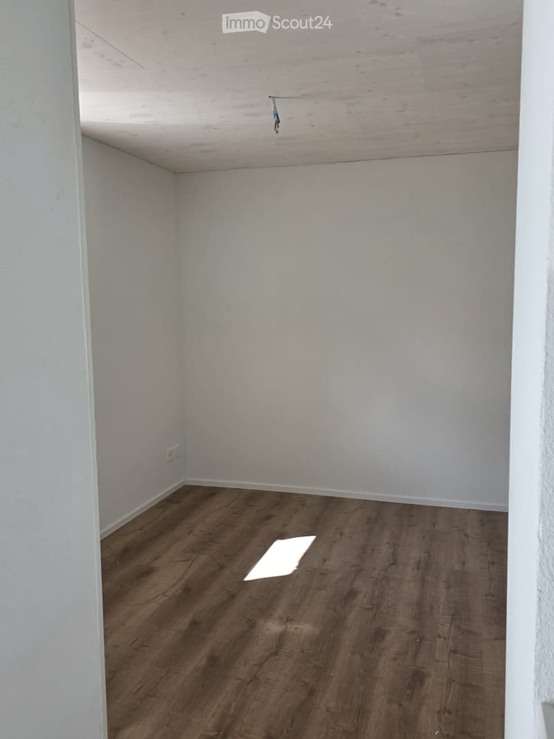 Empty room with wooden flooring and white walls, featuring a visible electrical outlet and a small piece of paper on the floor.