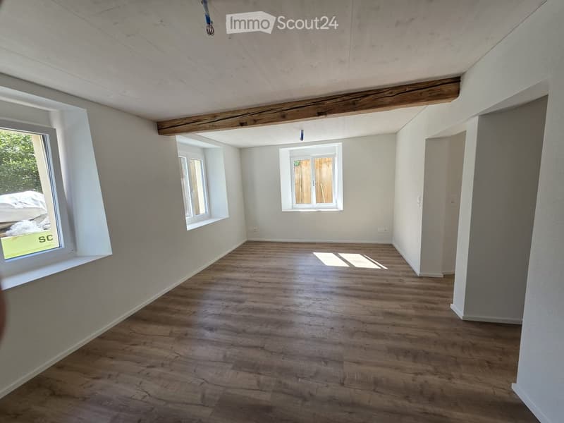 Empty room with wooden flooring, white walls, and multiple windows allowing natural light. Exposed wooden beams on the ceiling.