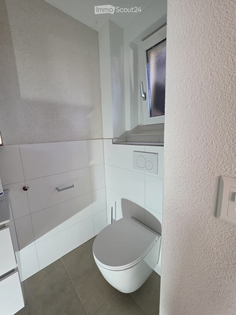 Modern bathroom with white tiles, a toilet, a mirrored cabinet, and a light switch on the wall.