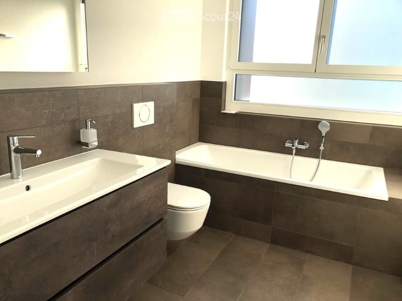 Modern bathroom with a white sink, chrome faucet, toilet, bathtub, and showerhead. Dark brown tiles on walls and floor, large window providing natural light.