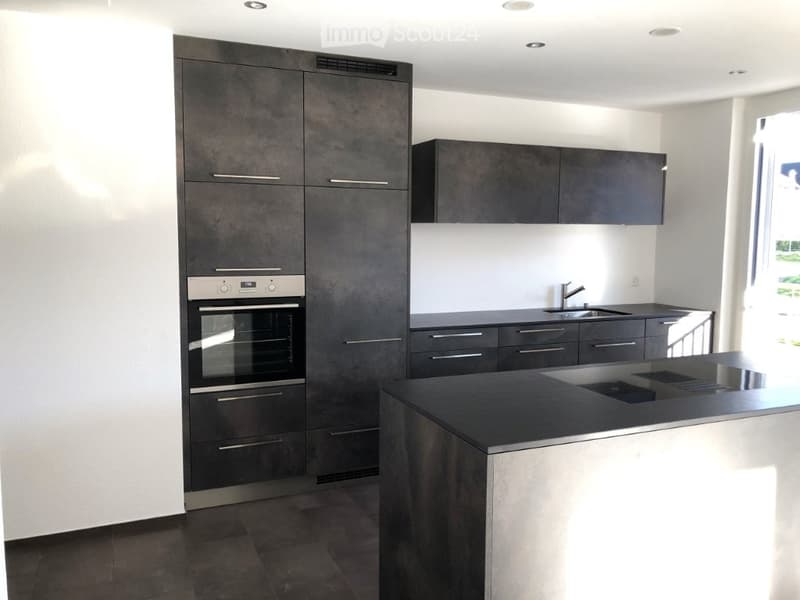 Modern kitchen with dark grey cabinets, stainless steel oven, and a central island with a black countertop.