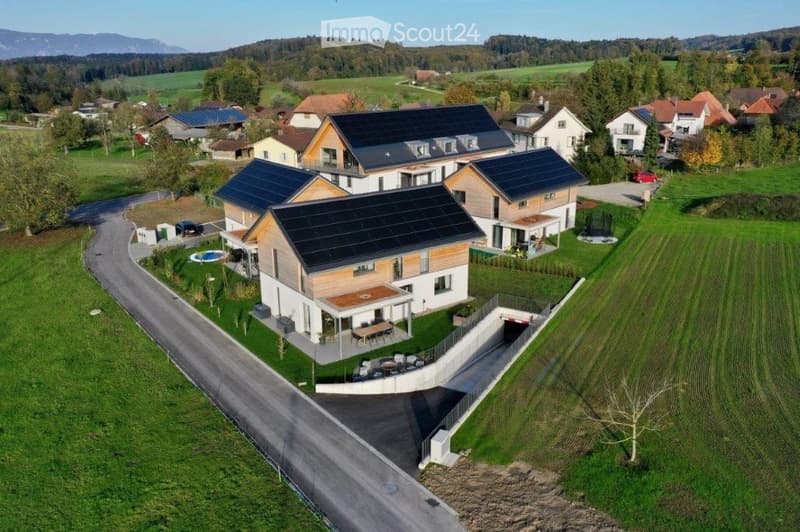 Aerial view of a modern, multi-story house with solar panels on the roof, surrounded by a well-maintained lawn, a swimming pool, and a parking area.