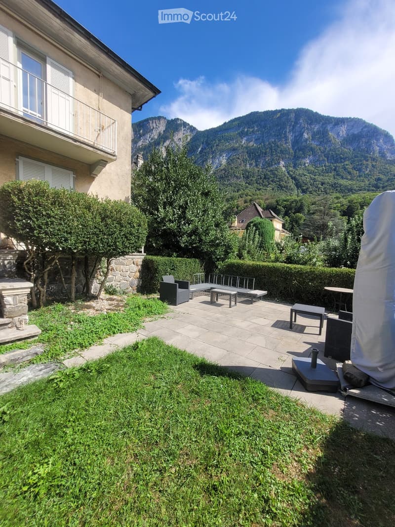 Garden with patio furniture, grassy area, and scenic mountain view.