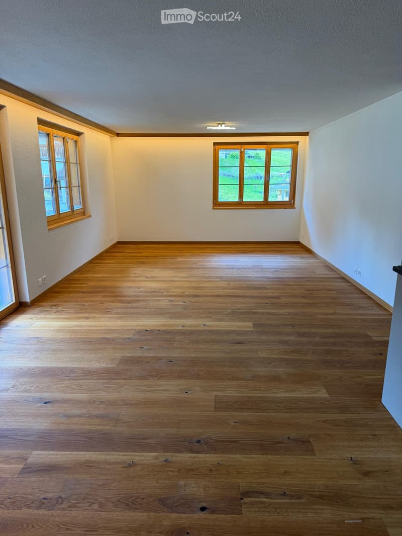 Empty room with wooden flooring, light-colored walls, and multiple windows with wooden frames. No furniture or equipment is present.