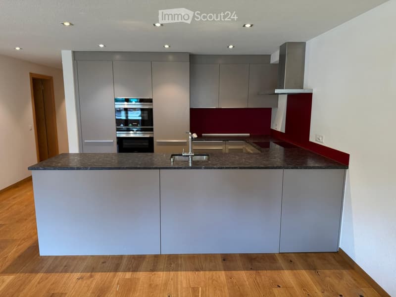 Modern kitchen with grey cabinets, a dark countertop, a sink with a faucet, and an oven in the background.