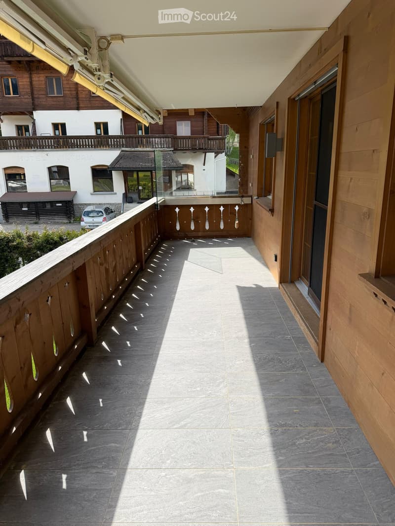 Balcony with wooden railings, tiled floor, and a view of the surrounding buildings and greenery.