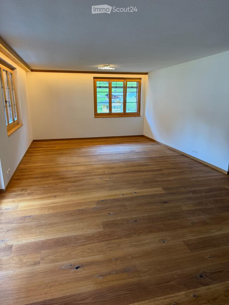 Empty room with wooden flooring, white walls, and large windows with wooden frames. No furniture or equipment present.