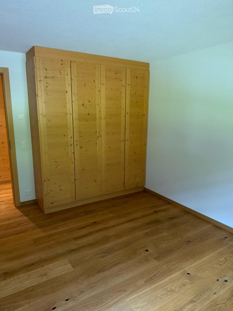 Empty room with light wooden flooring and a large wooden wardrobe with multiple doors.