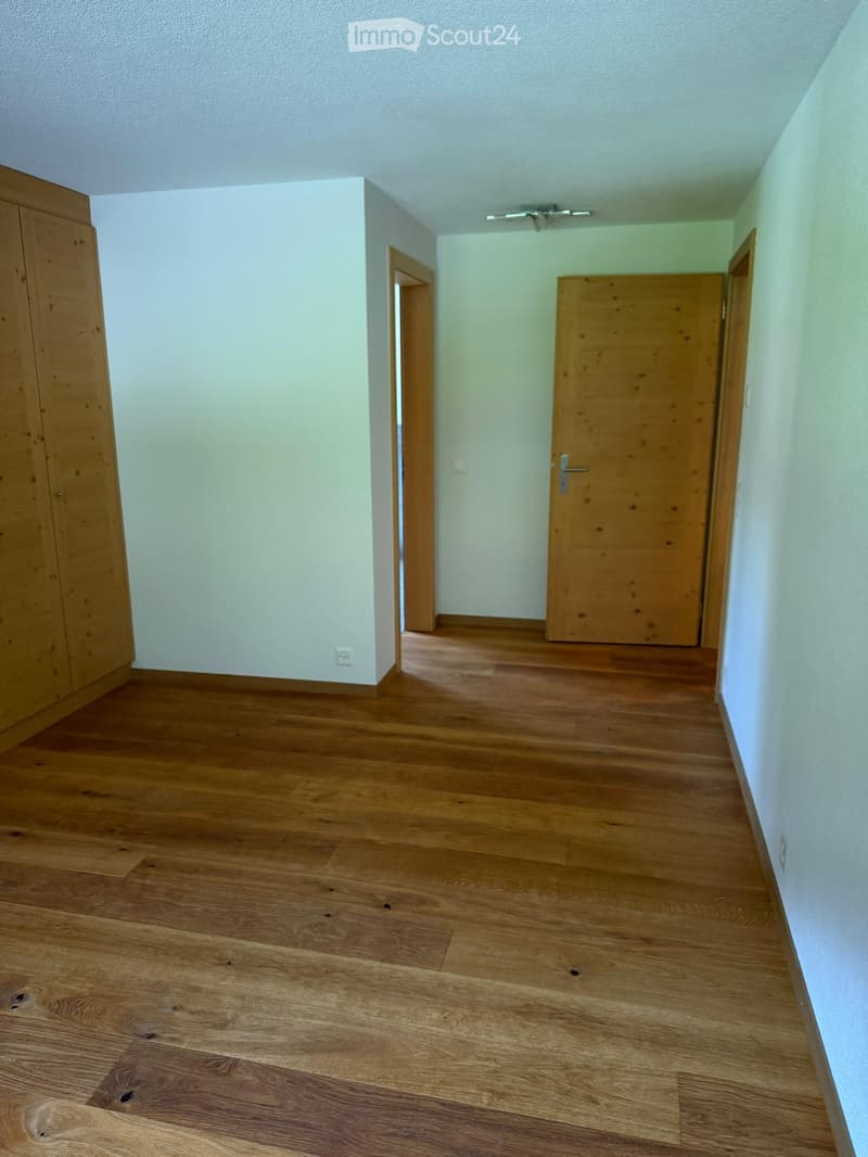 Empty hallway with wooden flooring, light-colored walls, and two wooden doors.