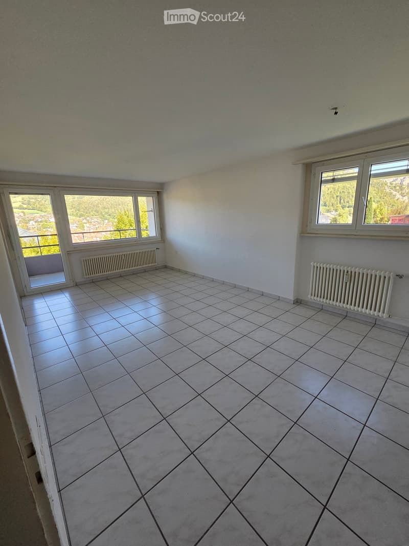 Empty room with tiled floor, white walls, large windows, and radiators. No furniture or equipment present.