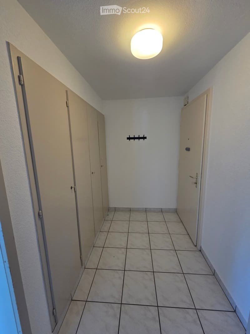Empty hallway with tiled floor, white walls, and two closed doors on either side. A round ceiling light fixture is visible at the end of the hallway.