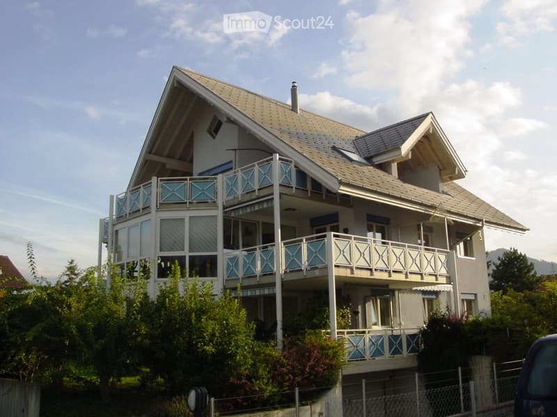 Two-story house with multiple balconies, large windows, and a sloped roof.