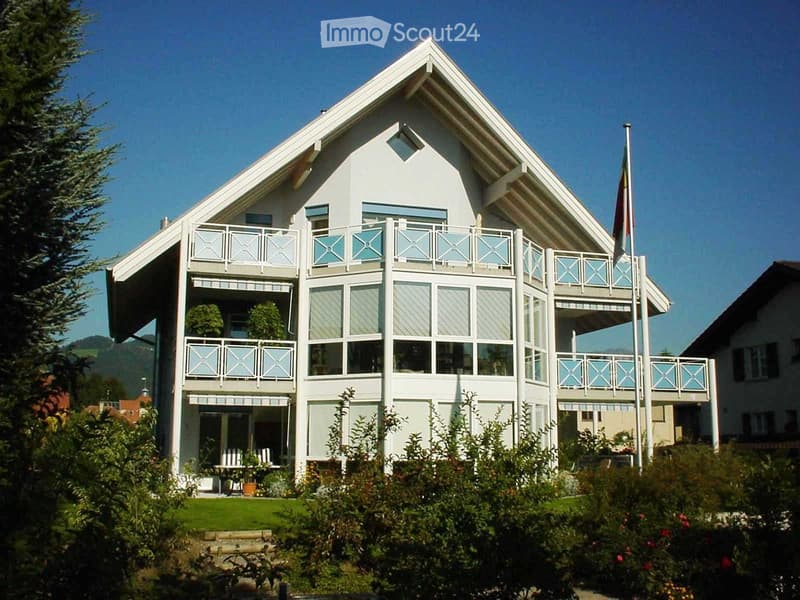 Two-story white house with multiple balconies, large windows, and a well-maintained garden.