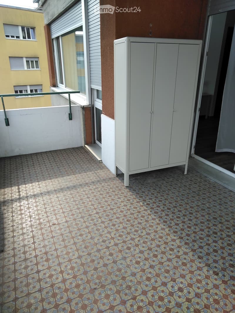 Balcony with patterned tile floor, white cabinet, metal railing, and adjacent building windows.