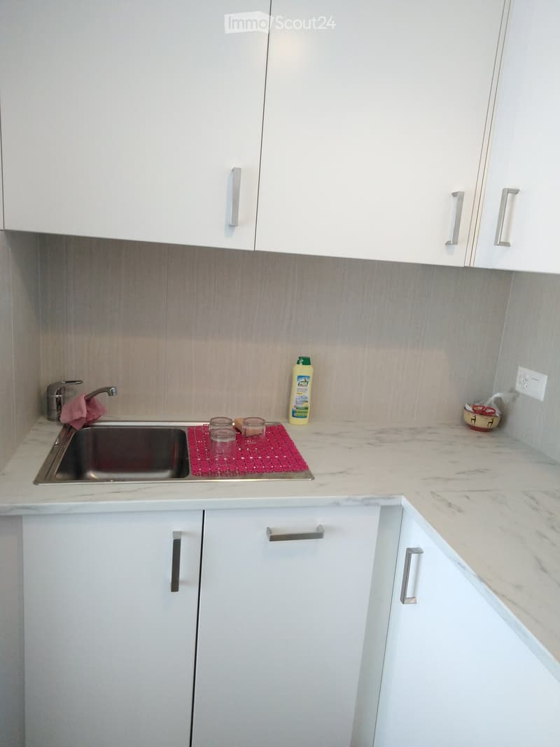 Modern kitchen with white cabinets, marble countertops, and stainless steel sink.