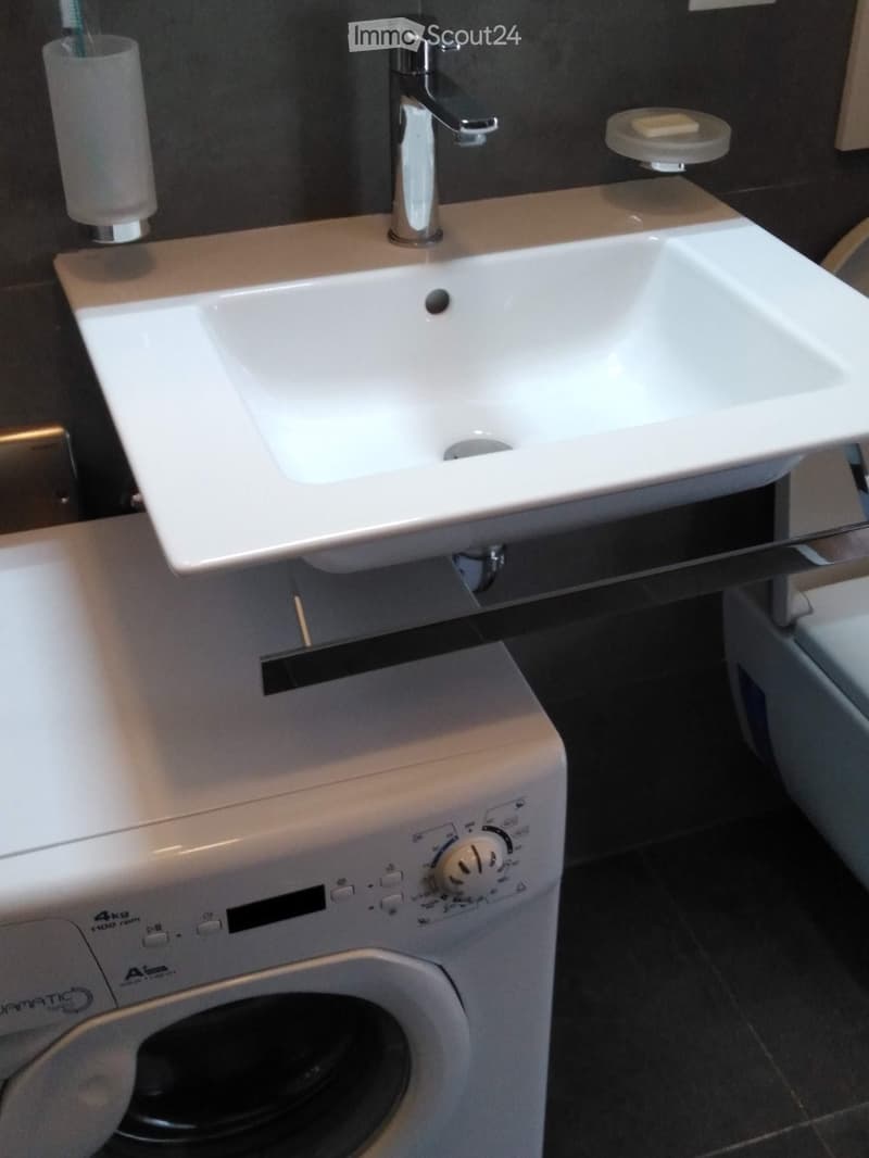 Modern bathroom with a white sink, chrome faucet, toothbrush holder, soap dish, and a white washing machine.