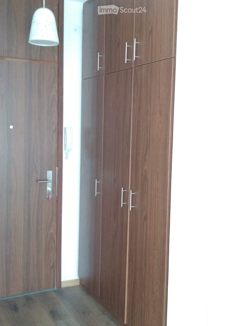 Empty room with wooden wardrobe and a hanging light fixture. The floor is tiled, and the walls are painted white.