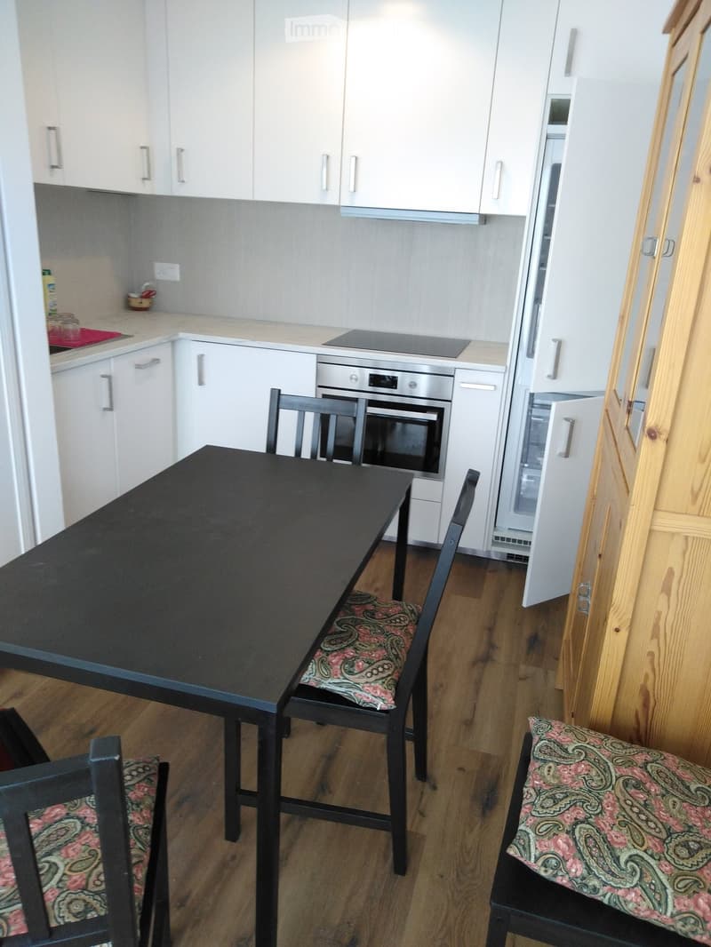 Modern kitchen with white cabinets, stainless steel appliances, a black dining table with four chairs, and a wooden floor.