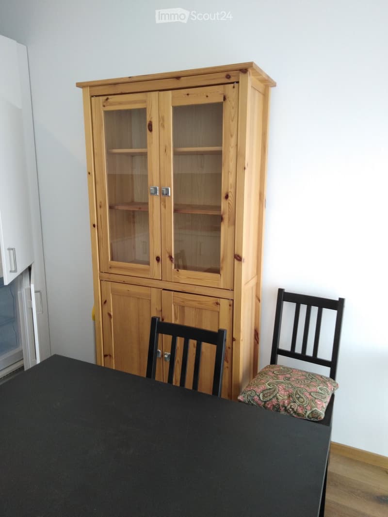 Dining area with a black table, two black chairs, and a wooden cabinet with glass doors.