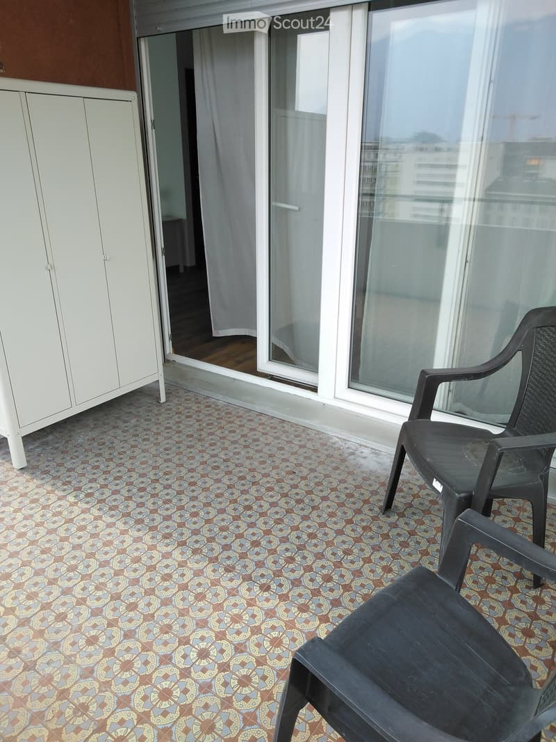 Balcony with patterned tile floor, two black plastic chairs, and an open door leading to an interior space.