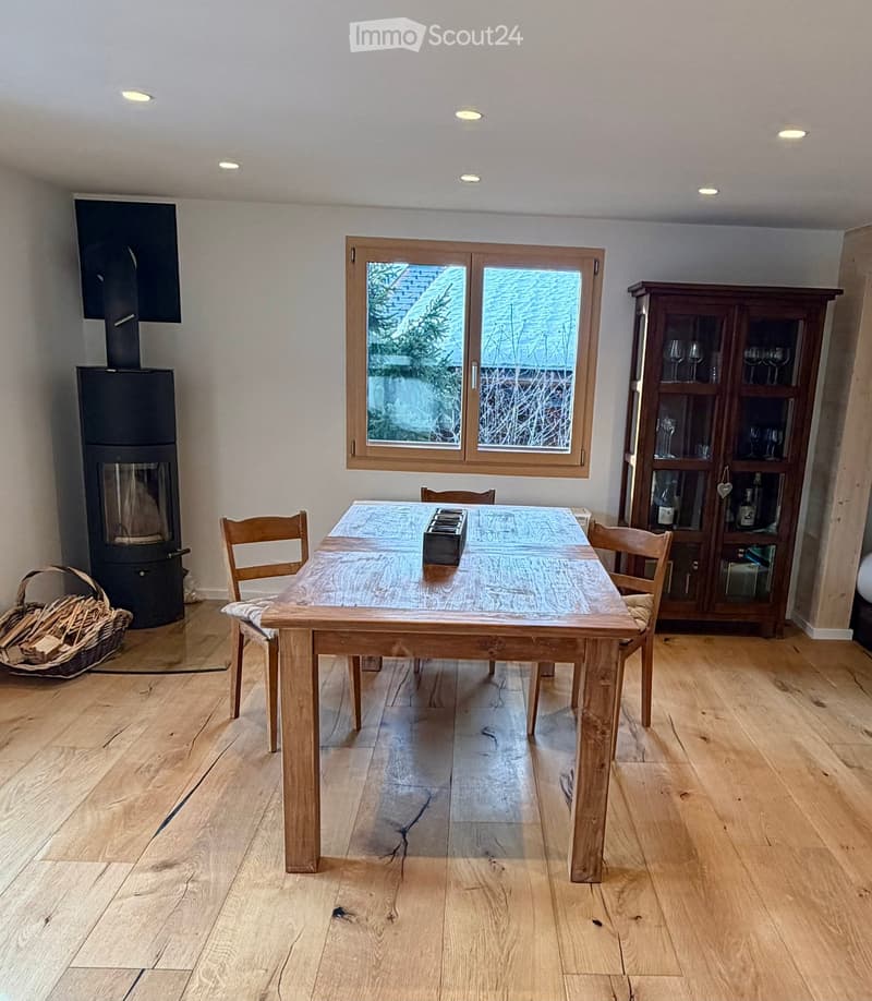dining area with a wooden table, chairs, a basket for firewood, a black wood-burning stove, a glass cabinet, a wooden floor, and recessed lighting