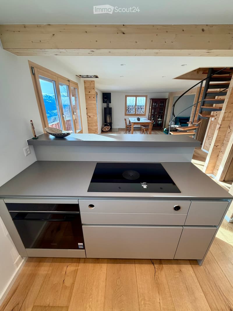 Modern kitchen with induction stove, built-in oven, wooden floor, and an open view to the dining area.