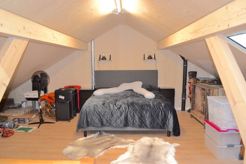 Cozy attic bedroom with wooden slanted ceilings, a large bed with grey bedding, nightstands, a fan, and storage boxes.