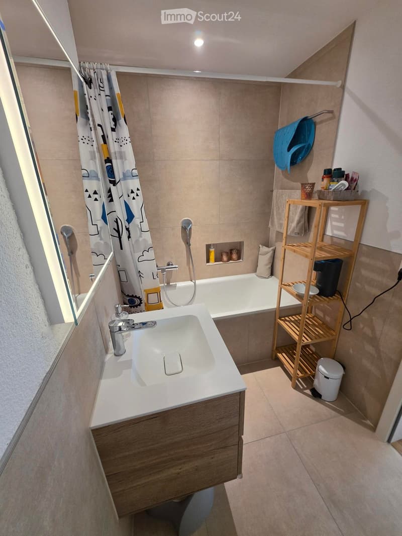 Modern bathroom with a white sink, bathtub, wooden shelf, and various toiletries.