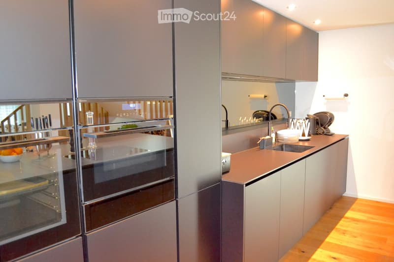 Modern kitchen with sleek, grey cabinets, a stainless steel oven, a sink with a modern faucet, and a countertop with a coffee maker and other small appliances.