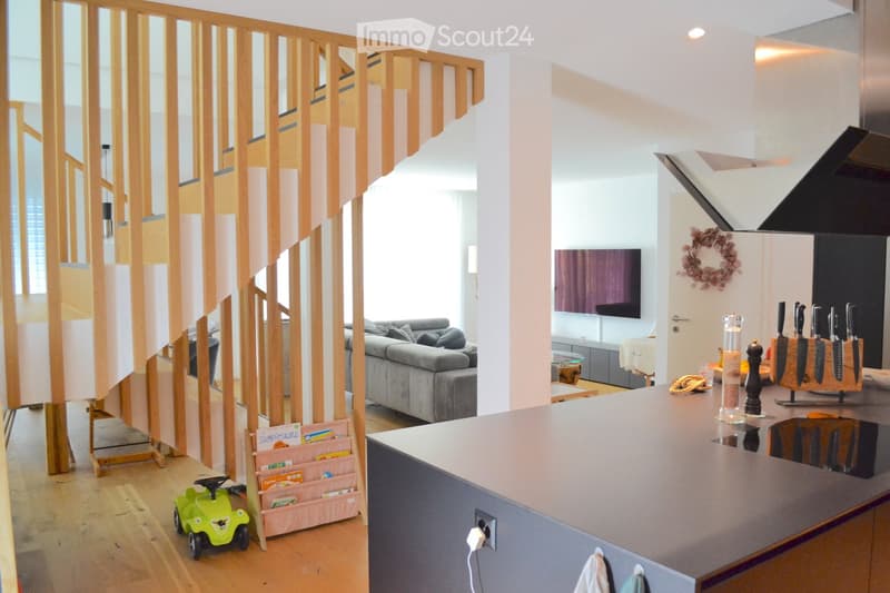 Open-plan living and dining area with a grey sofa, coffee table, flat-screen TV, kitchen counter, and decorative items including a knife block and a toy car.