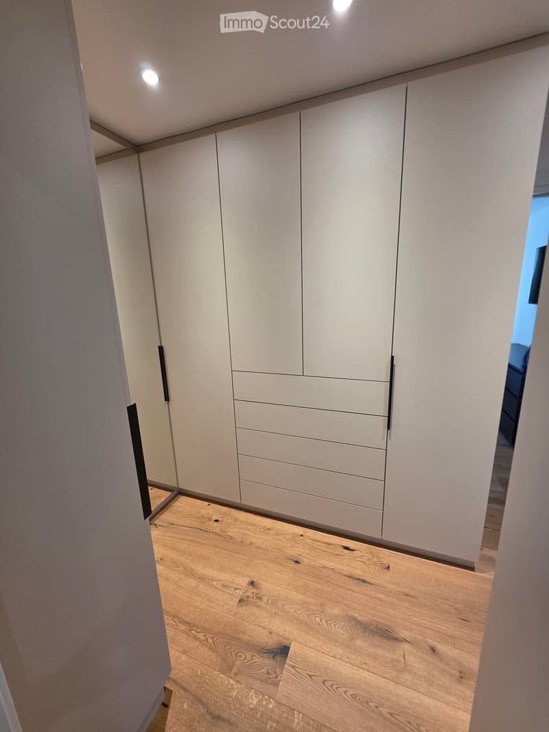 Empty hallway with light wooden flooring and white built-in wardrobes with multiple drawers and doors.