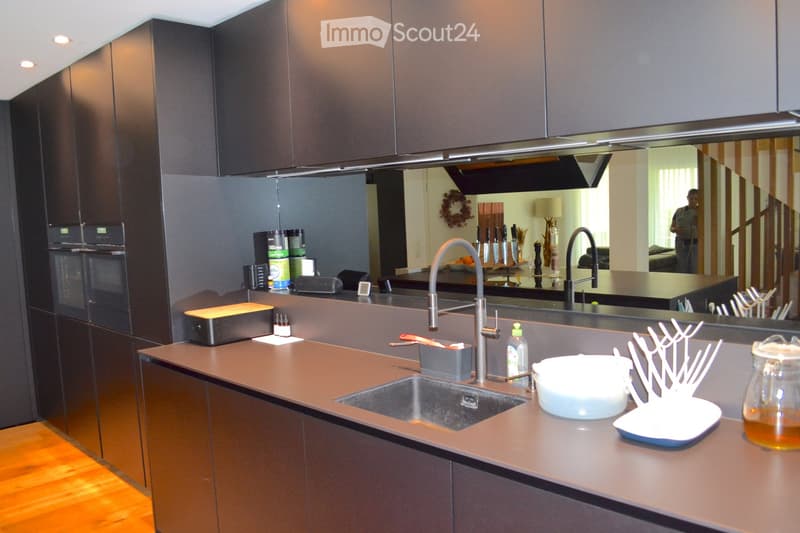 Modern kitchen with dark wood cabinets, stainless steel sink, and various appliances. Countertop features a bowl, dish rack, and other small items.