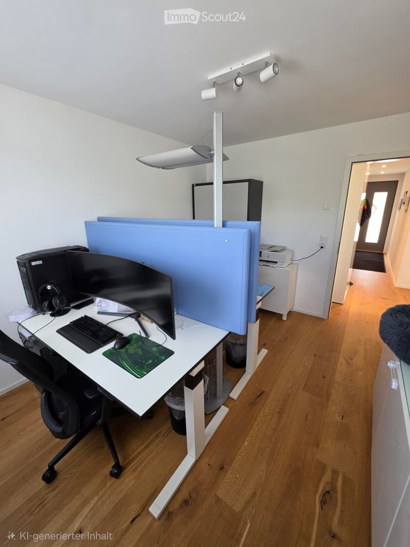 Modern office space with a white desk, ergonomic chair, dual monitors, keyboard, mouse, and a large screen divider. Wooden flooring and track lighting are visible.