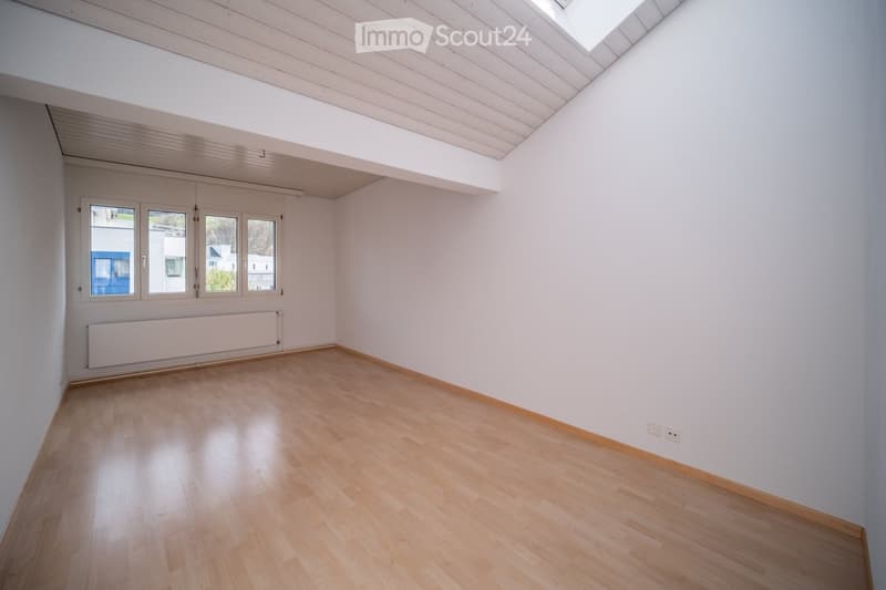 Empty room with light wooden flooring, white walls, large windows, and a skylight in the ceiling.