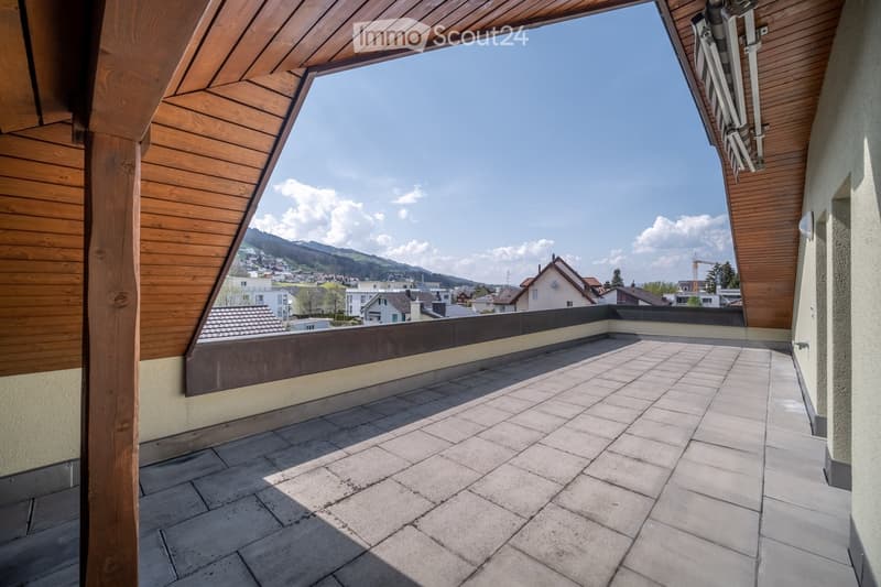 Roof terrace with tiled flooring, wooden railings, and scenic mountain and town views.