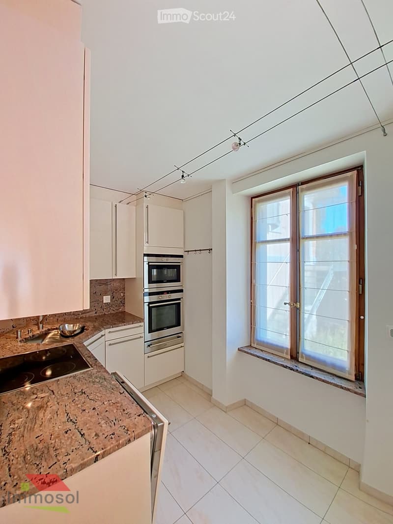Modern kitchen with white cabinets, stainless steel appliances, granite countertop, and a large window with blinds.
