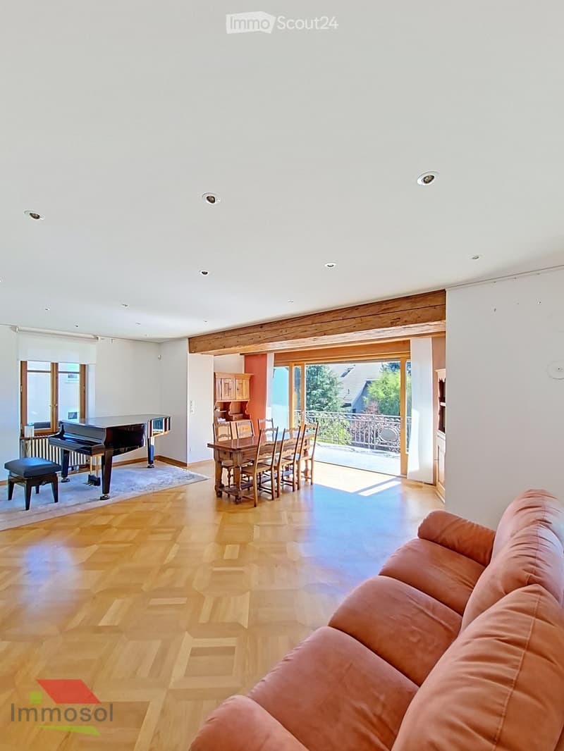 Spacious living area with wooden flooring, a pink sofa, a grand piano with a matching bench, a dining table with chairs, and a cabinet, connected to a balcony.