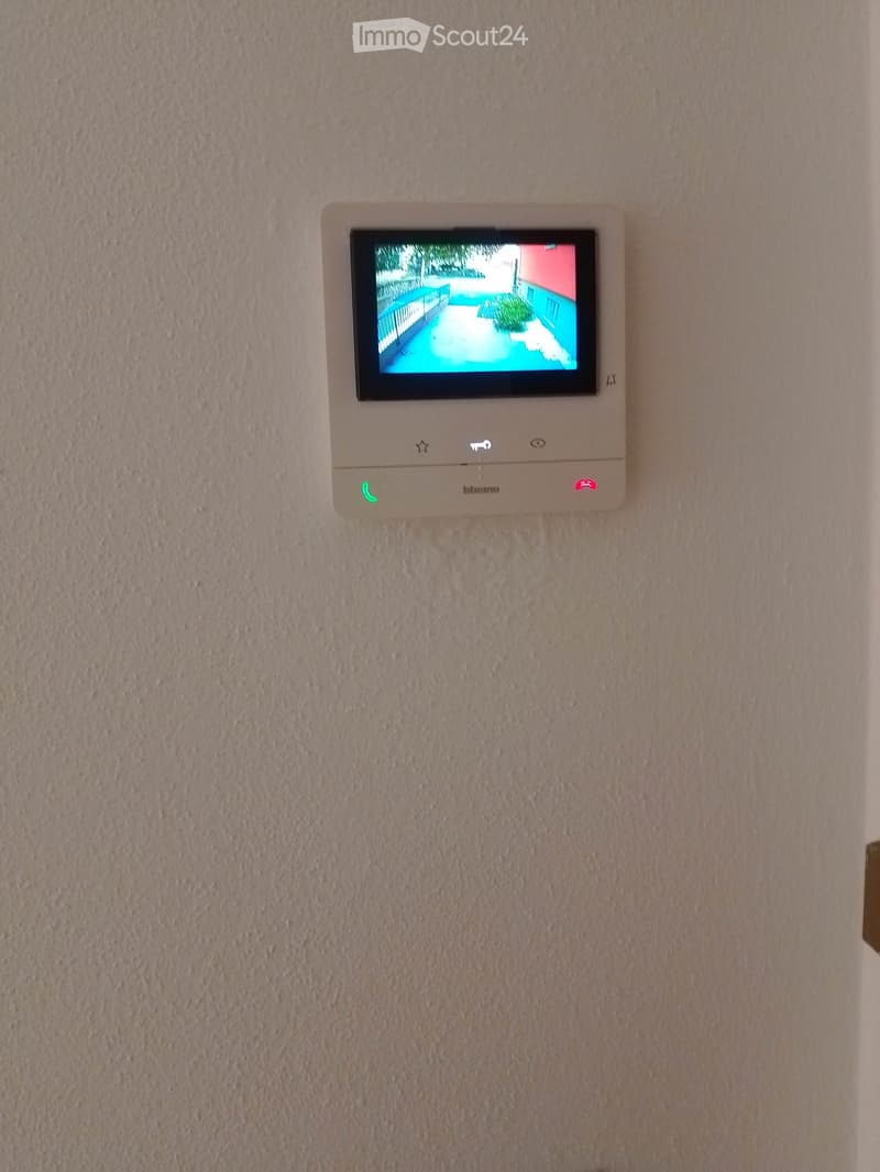 A wall-mounted security camera system displaying a live feed of an outdoor area, including a swimming pool and surrounding structures.