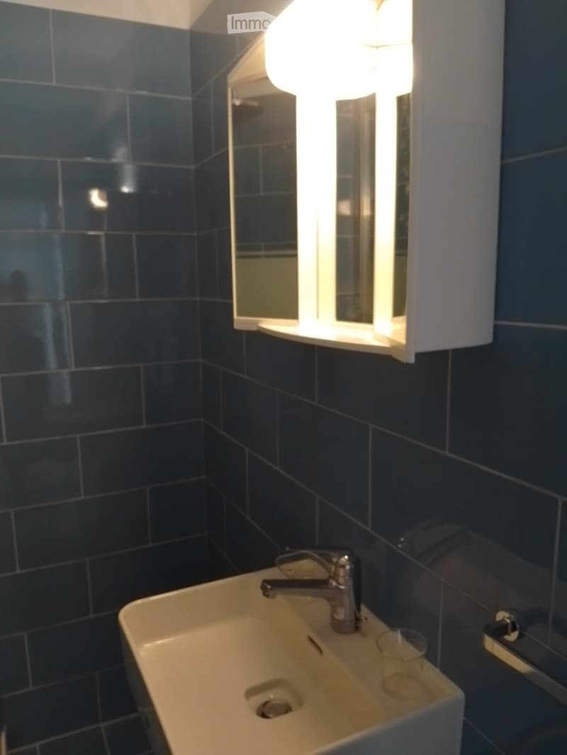 Bathroom with dark tiled walls, a white sink with a chrome faucet, a mirror with built-in lighting, and a small glass cup on the sink.