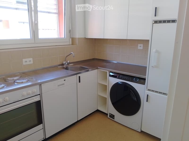 Compact kitchen with white cabinets, stainless steel sink, oven, dishwasher, and washing machine.