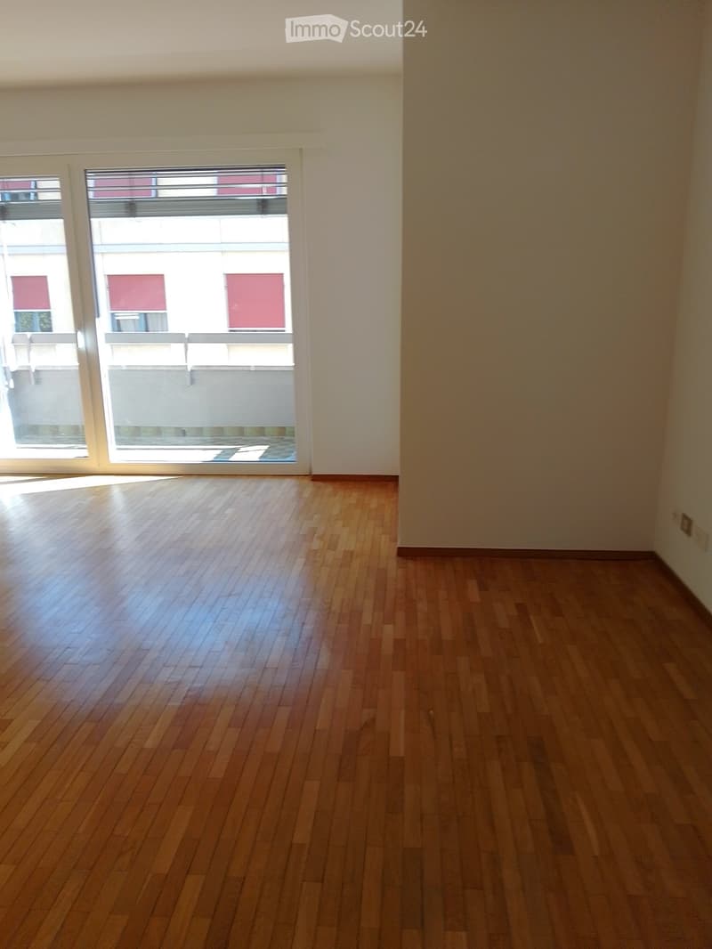 Empty room with wooden flooring and large windows, allowing natural light to fill the space.
