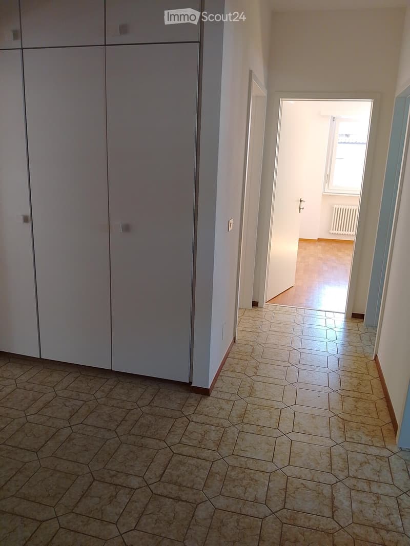 Empty hallway with hexagonal tiled floor, white walls, and a closed door on the left leading to another room.